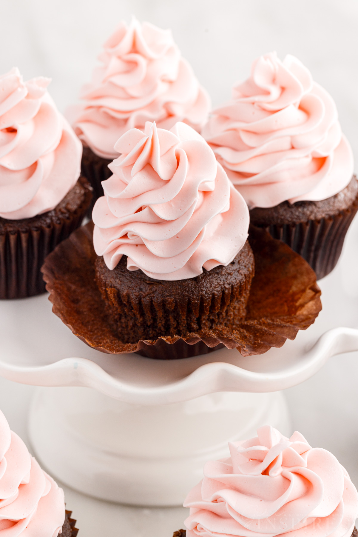 Four chocolate cupcakes topped with big swirls of strawberry frosting on a cake platter.
