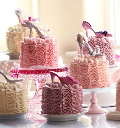pink ruffle cakes on various plates and cake stands on a table. Cakes each have miniature shoe decoration on top
