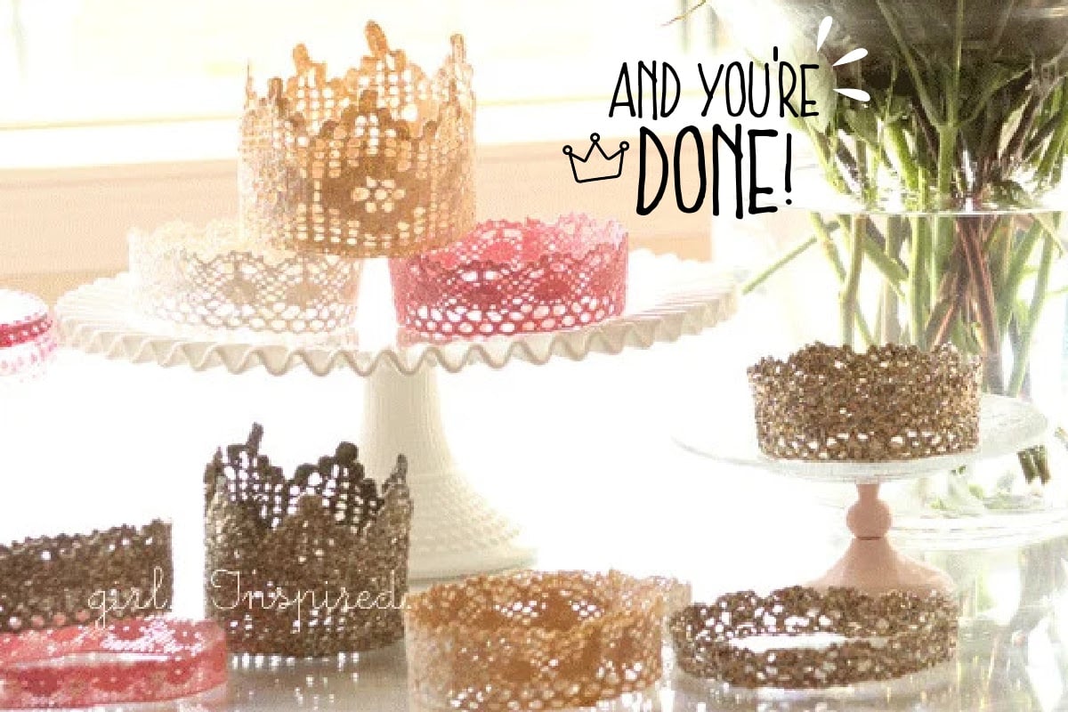 A variety of DIY princess crowns in various colors and shapes set on a table and cake platter, in front of vase of flowers.