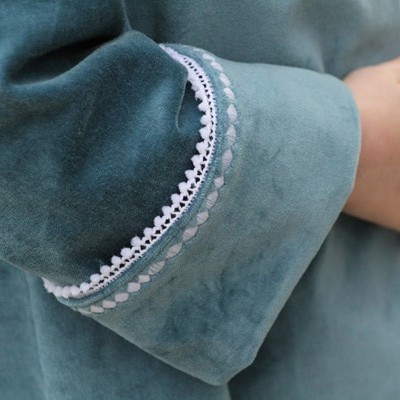 close up of cuffed coat sleeve in teal velveteen with white pom pom trim