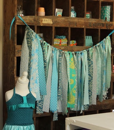 strips of various blue fabrics tied on ribbon hanging across cubby furniture