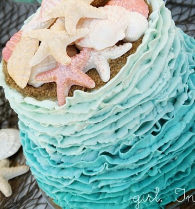 ruffly blue icing covering two tiered cake with candy seashells on top and brown sugar "sand"