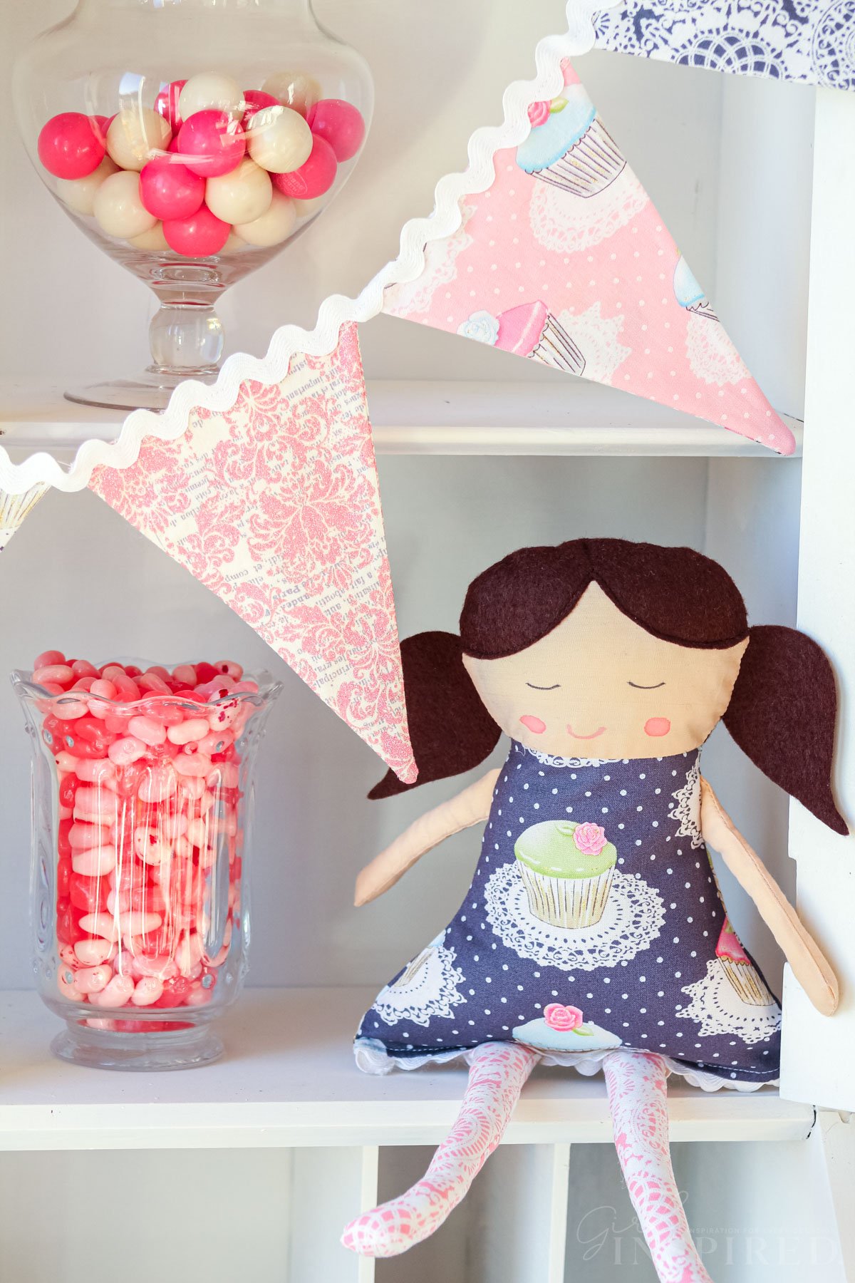 Fabric doll set on shelf next to fabric pennant banner and jar of jelly beans.