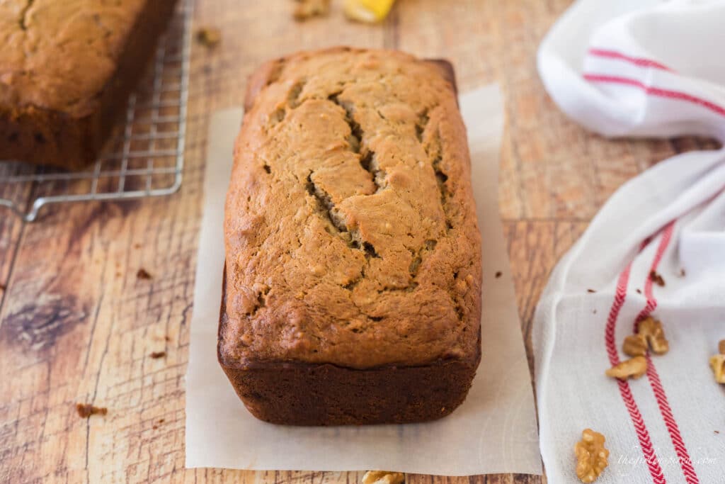 banana nut bread loaf next to cooling rack, with banana peel and tea towel