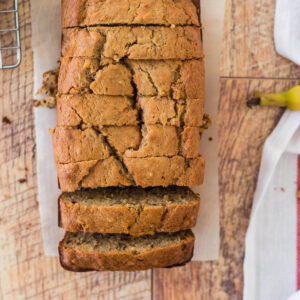 sliced banana nut bread loaf next to cooling rack, with banana peel and tea towel