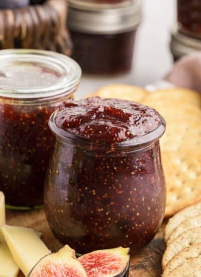 Balsamic fig jam in mason jars, surrounded by crackers, fresh fruit, nuts, cheese, and deli meat.