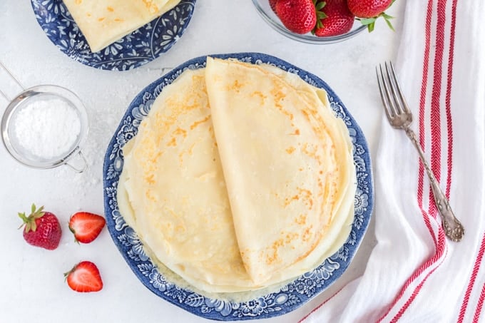 stack of round crepes on blue plate, strawberries to the side