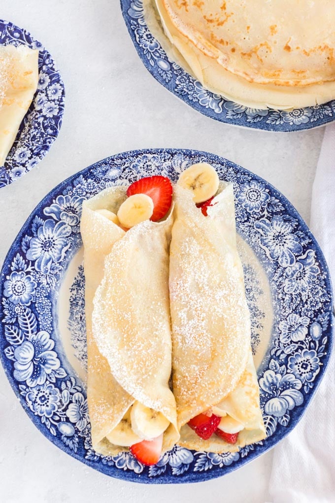 two crepes rolled with bananas and strawberries inside on a blue plate
