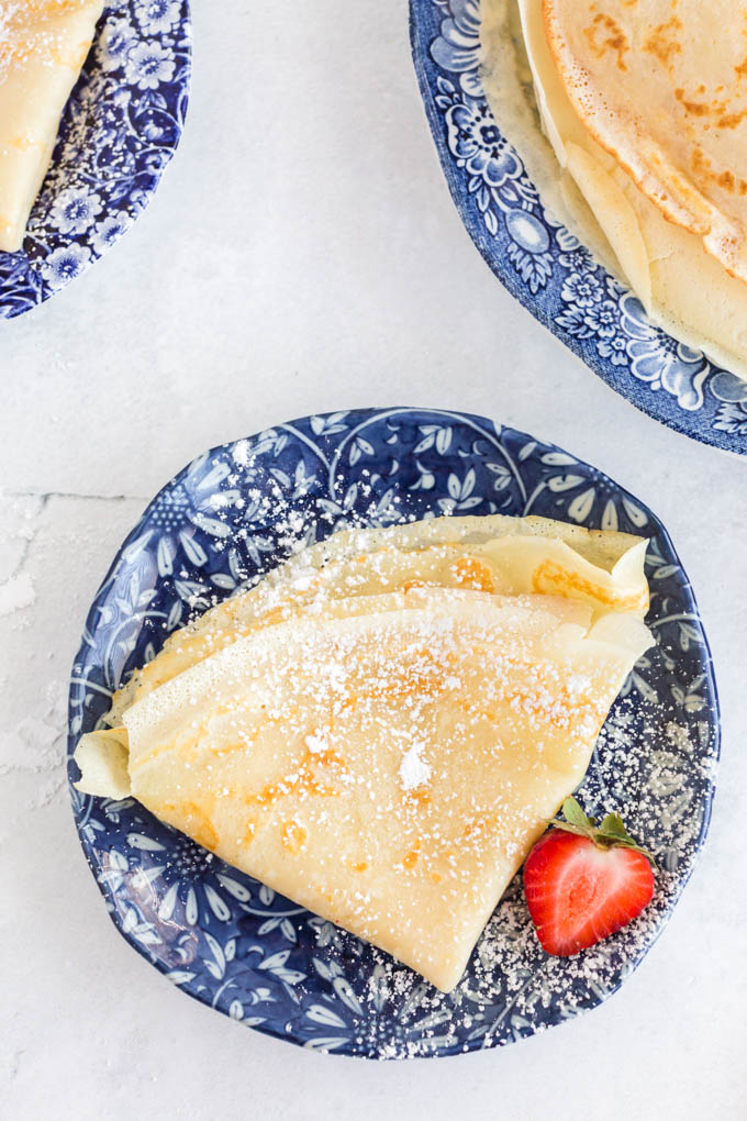 crepes folded in half and then in half again, stacked on blue plate with strawberry garnish