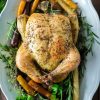 whole roasted chicken on white platter with rainbow carrots and fresh herbs