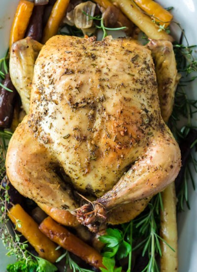 whole roasted chicken on white platter with rainbow carrots and fresh herbs