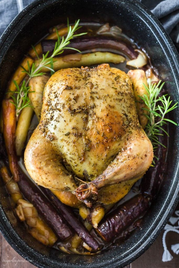 whole roasted chicken in black roasting pan with rainbow carrots and fresh herbs