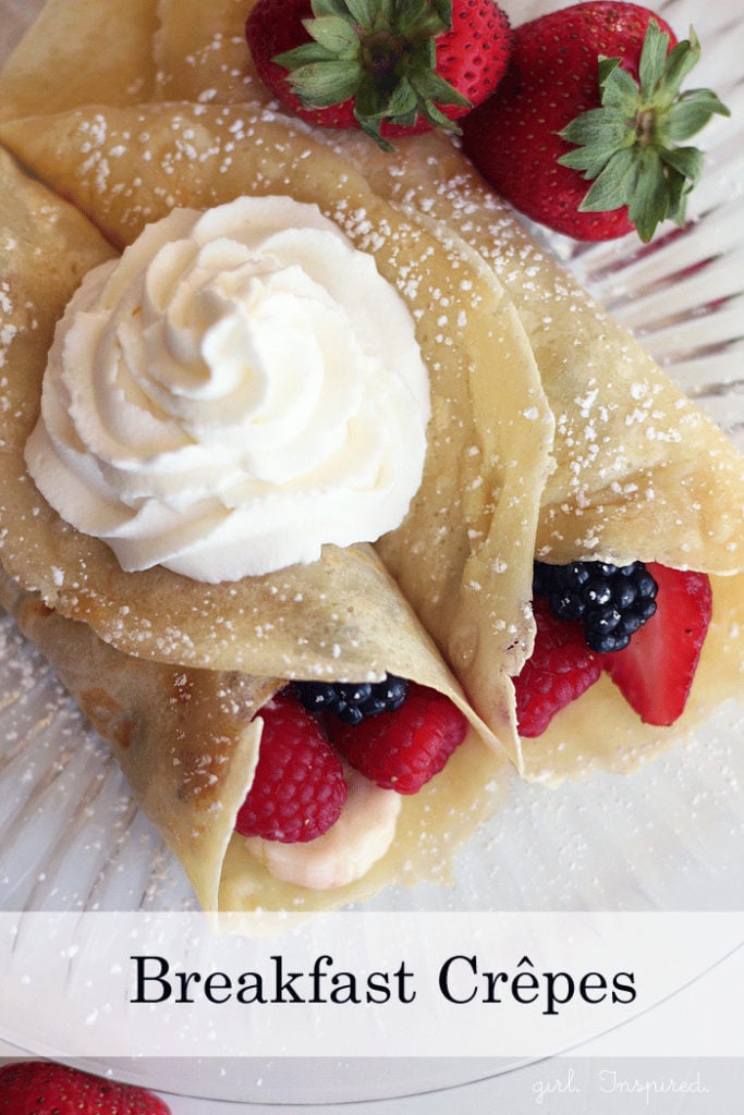 rolled crepes with berries and bananas inside and whipped cream on top, on glass plate
