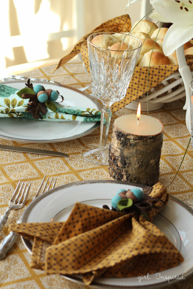 Table setting with gold and blue linens, a burning candle, and crafted felt blue acorns 