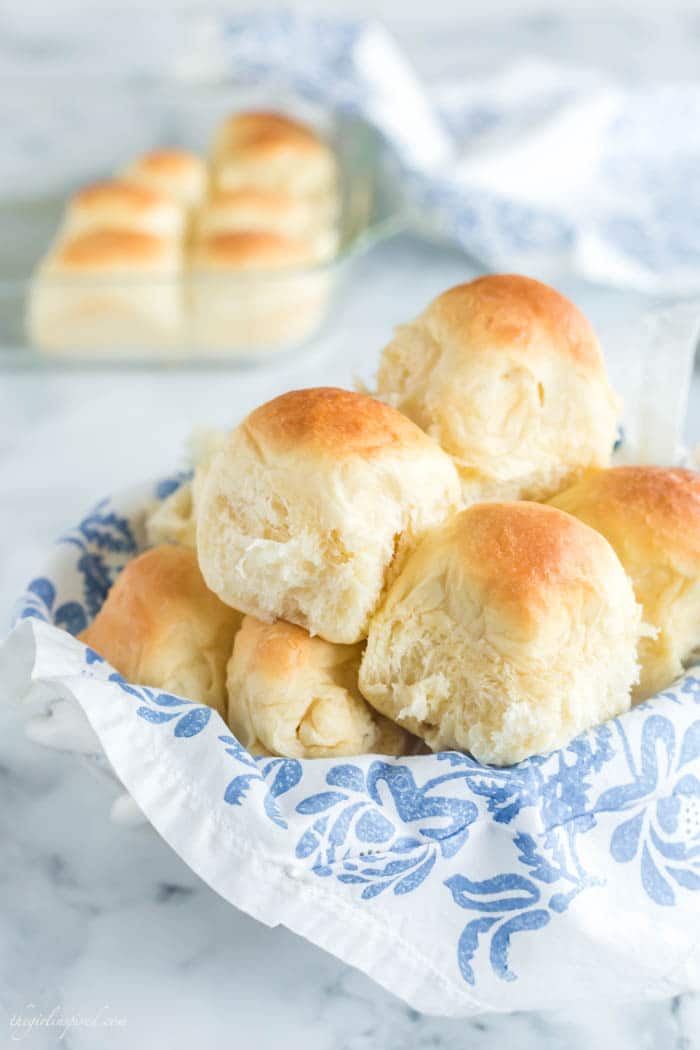 dinner rolls stacked in a bread basket with white and blue floral linen, baking dish with rolls