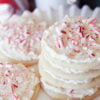 Cut-Out stacked sugar cookies with white frosting and pieces of candy cane on topugar Cookies topped with Peppermint Marshmallow Frosting and Candy Cane bits!
