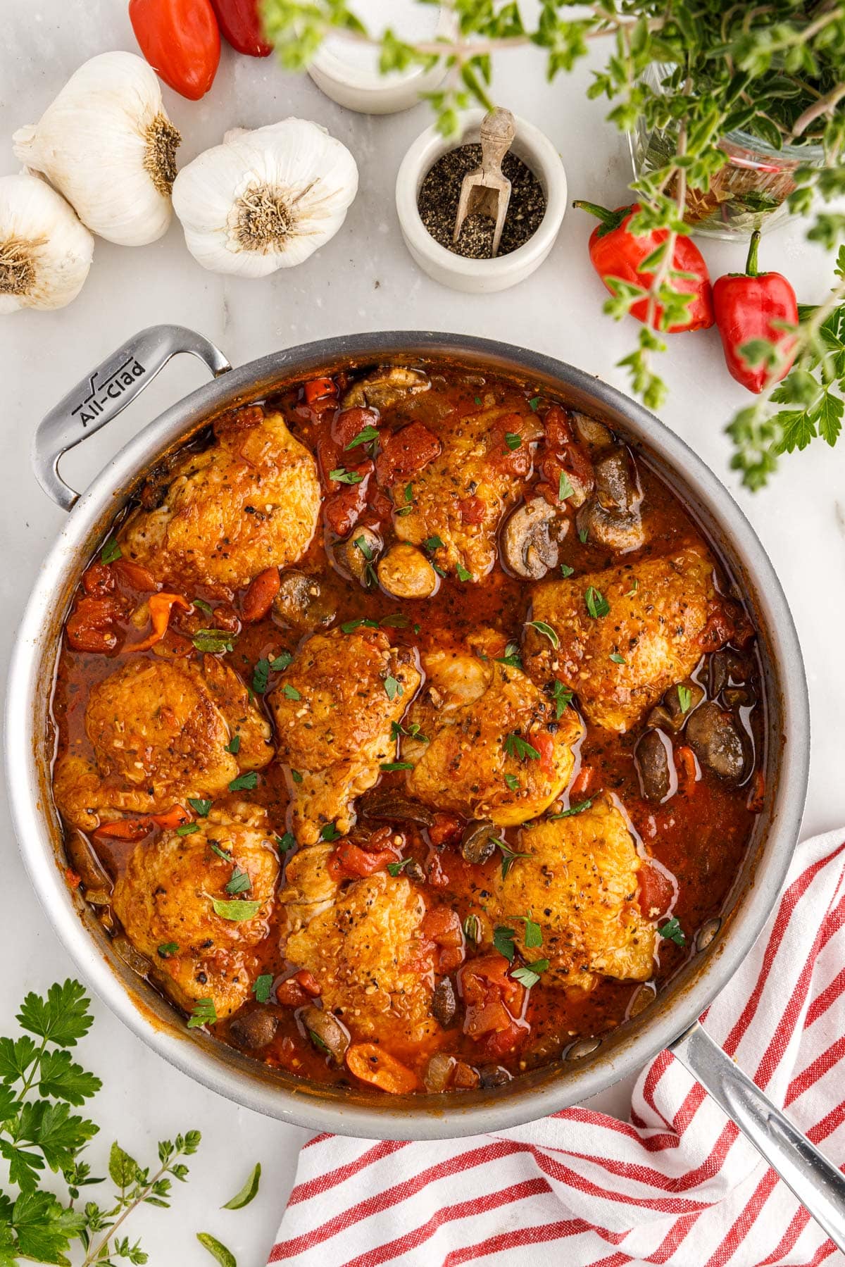 Skillet filled with chicken cacciatore, red striped linen, garlic and herbs.