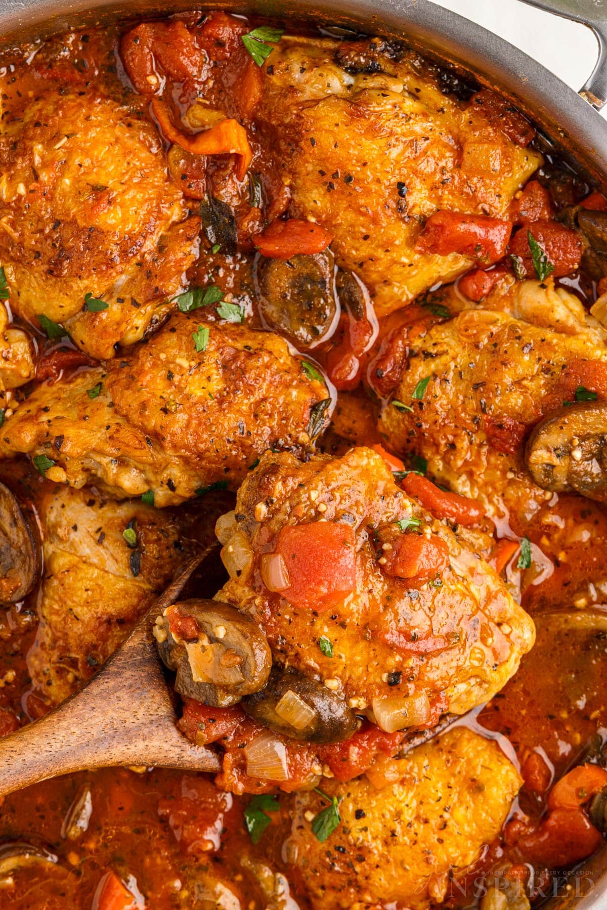 Spatula lifting a chicken thigh from pan of chicken cacciatore.