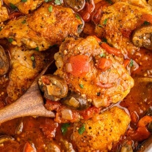 Spatula lifting a chicken thigh from pan of chicken cacciatore.