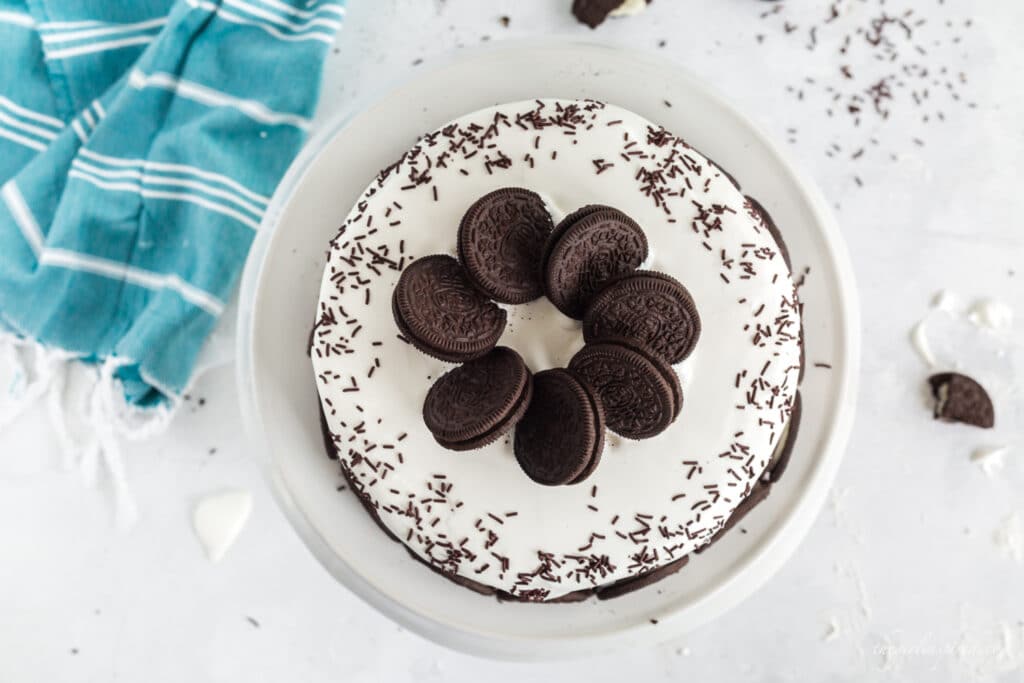 overhead photo of oreos and chocolate sprinkles on ice cream cake on white plate with aqua linen