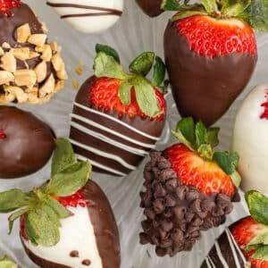 Platter of chocolate covered strawberries with a variety of coatings including crushed peanuts, white chocolate drizzle, mini chocolate chips, and plain dark chocolate.