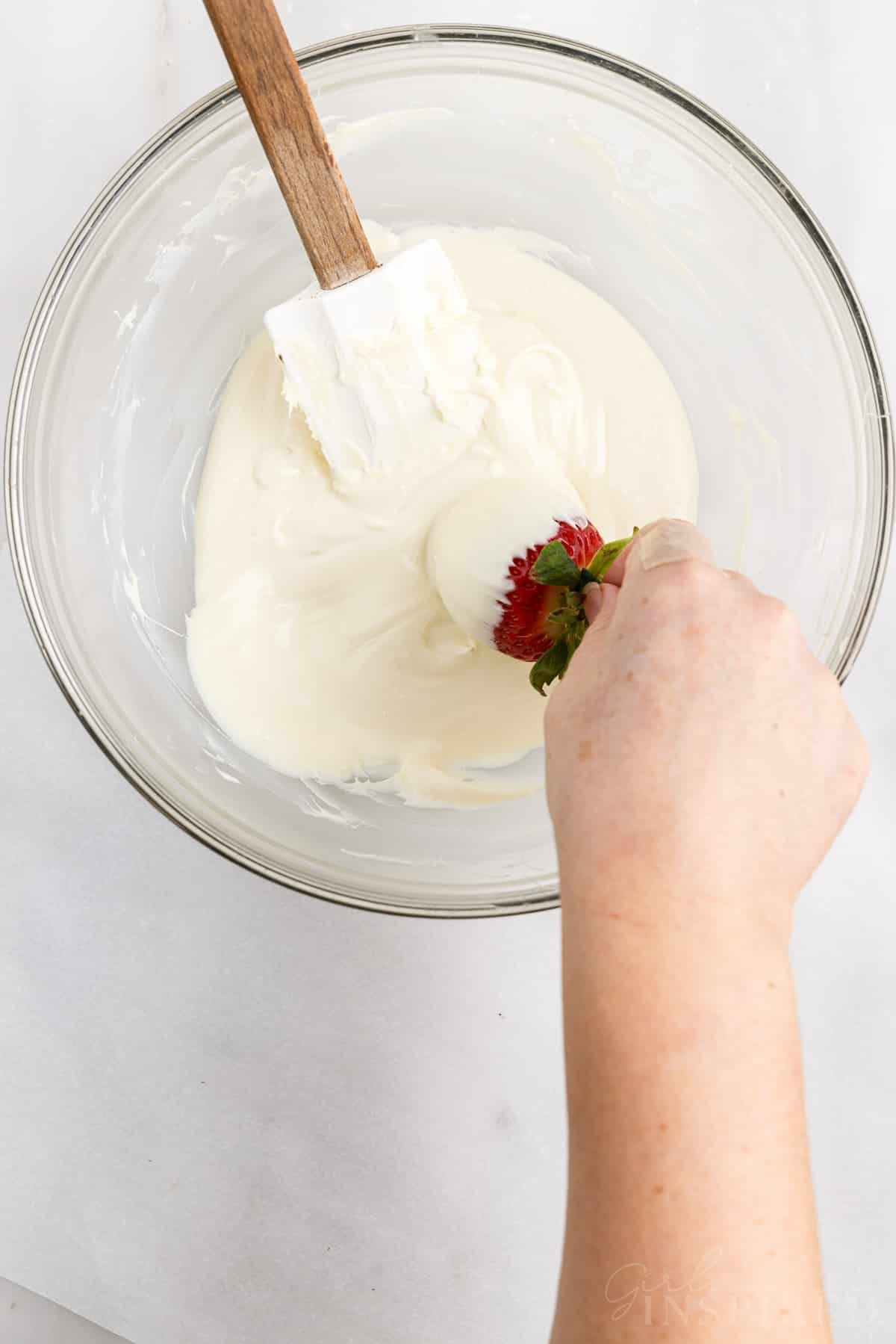 Dipping a whole strawberry into glass bowl of melted white chocolate.