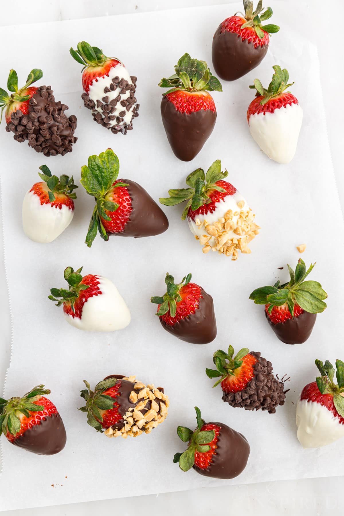 Sheet of parchment paper with chocolate covered strawberries dipped in a variety of coatings and toppings.