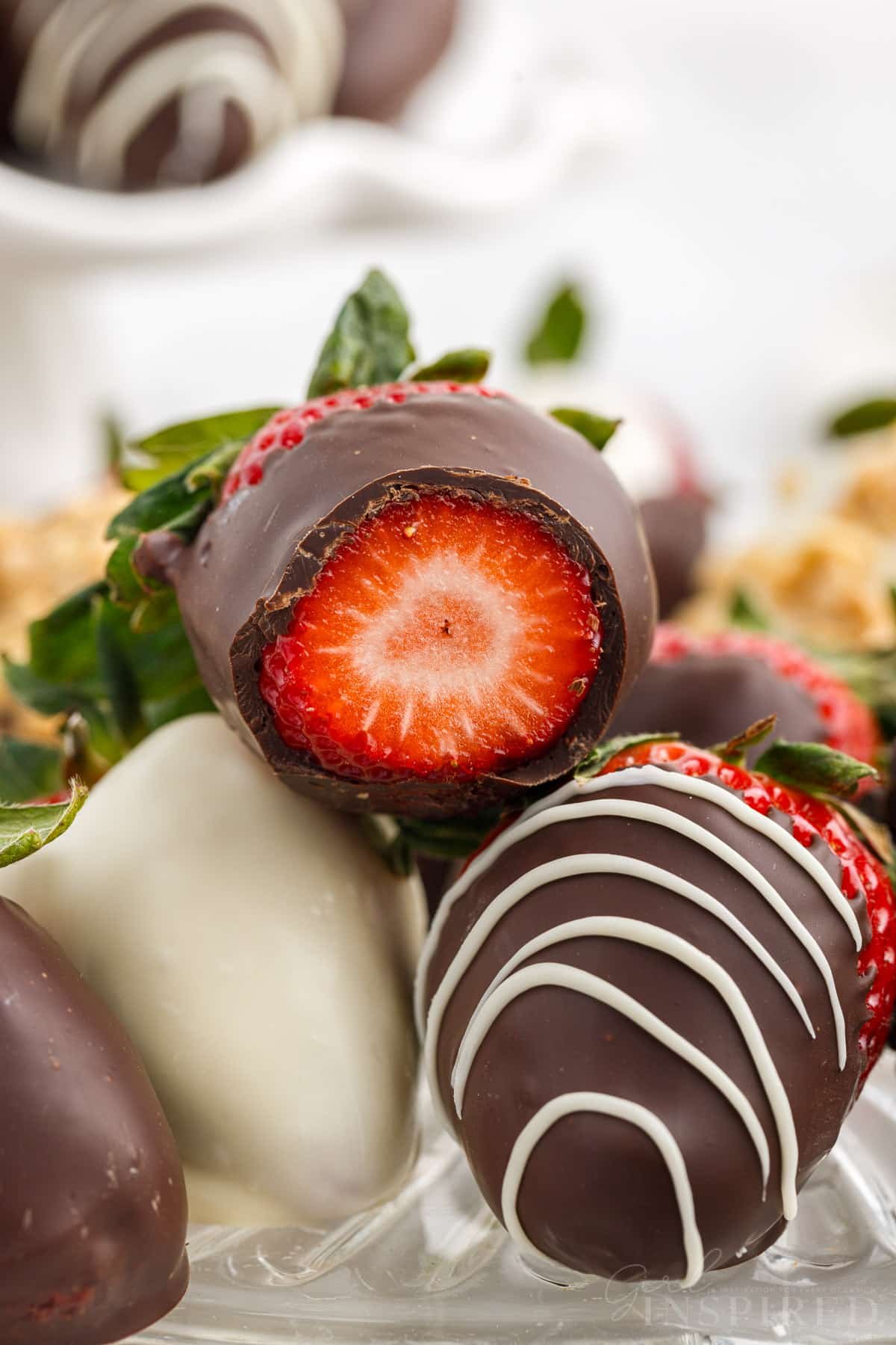 One chocolate dipped strawberry sliced open to show the inside stacked on top of a few other chocolate covered strawberries.