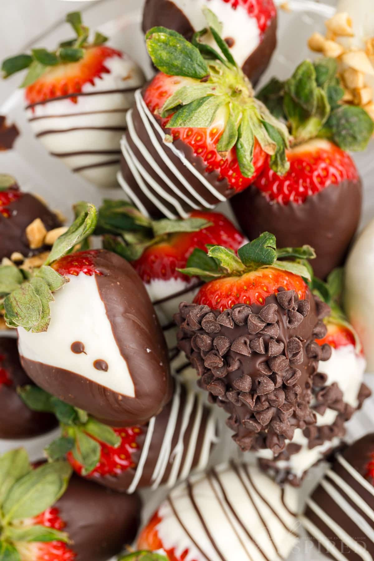 Stacked chocolate covered strawberries on a glass plate with a variety of toppings and decorations.