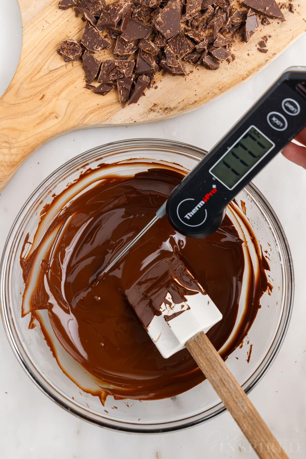 Melted chocolate in glass bowl with spatula and digital thermometer registering 117°F.