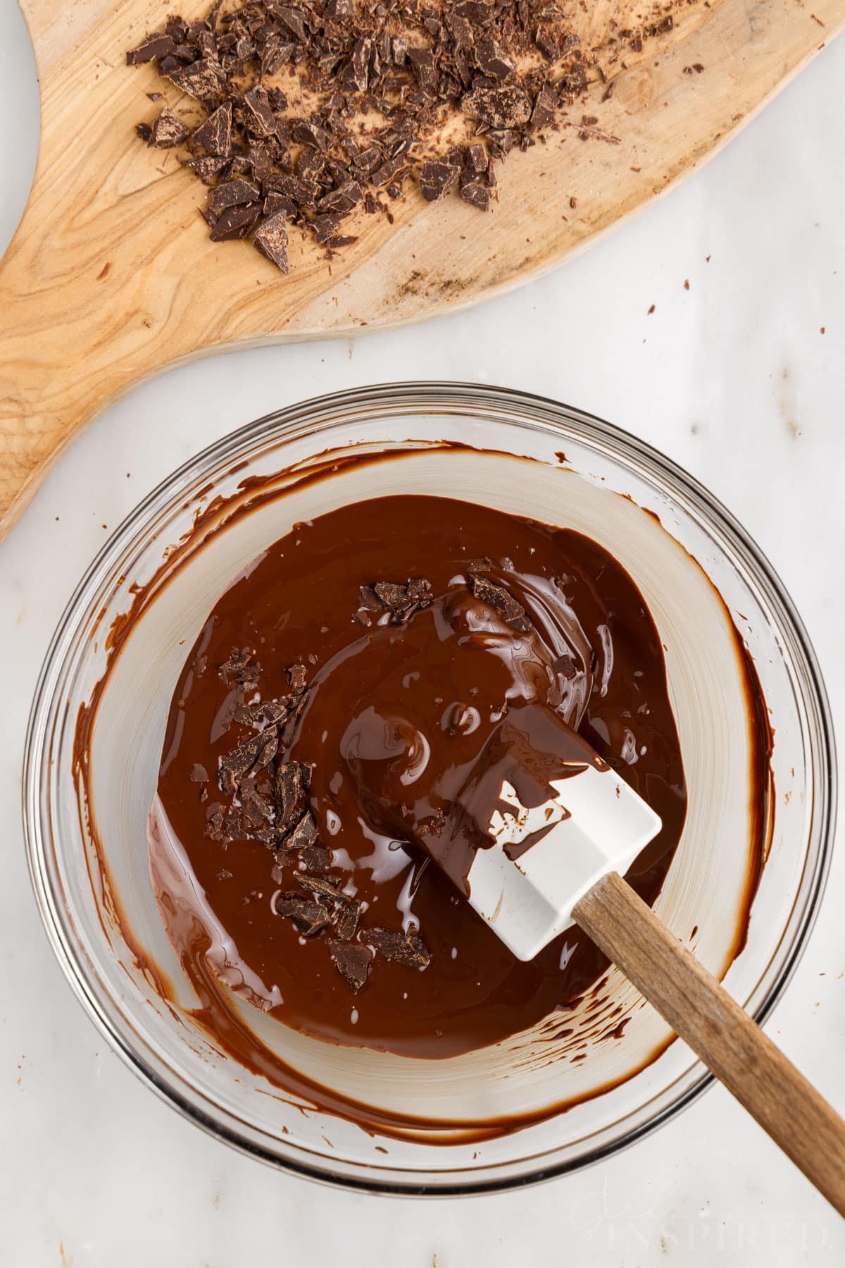 "Seed" chocolate pieces added to bowl of melted chocolate with spatula.