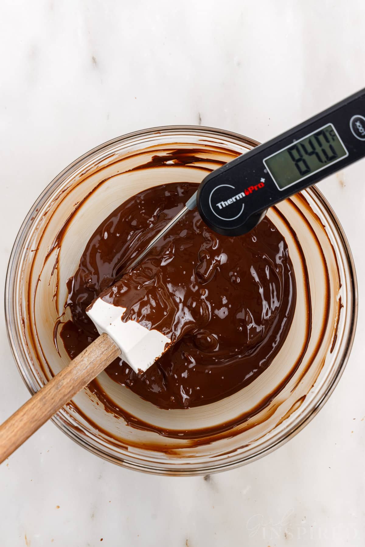 Digital thermometer and spatula in bowl of melted chocolate.