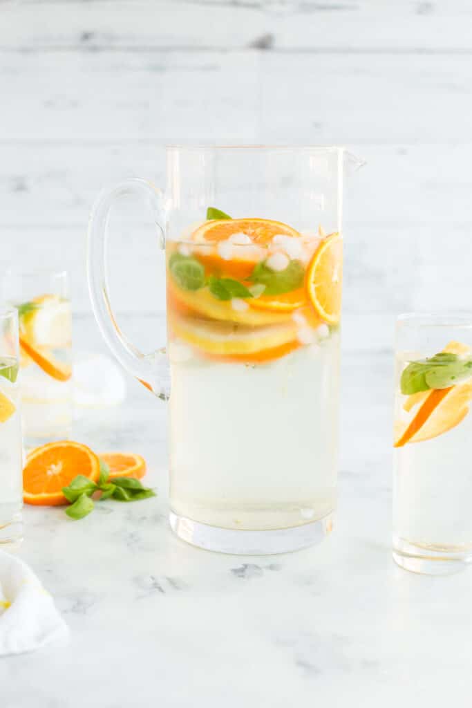 orange slices, lemon slices, and basil leaves with ice and water in glass pitcher and water glasses