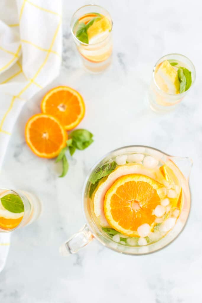 orange slices, lemon slices, and basil leaves with ice and water in glass pitcher and water glasses