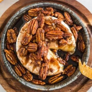 Brown sugar baked brie topped with brown sugar brandy pecans with a slice missing.