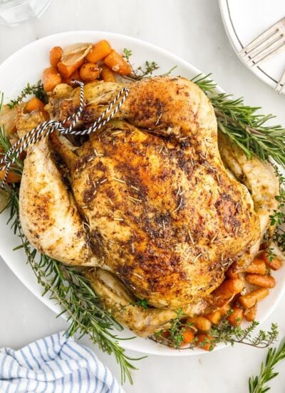 Whole herb roasted chicken garnished with rosemary on a large serving tray.