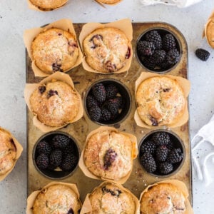 overhead view of blackberry muffins in muffin tin with some of the muffin spots filled with blackberries and a white linen