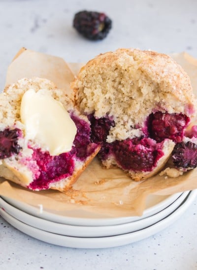 blackberry muffin on stack of white plates split open with butter in the middle and blackberries around