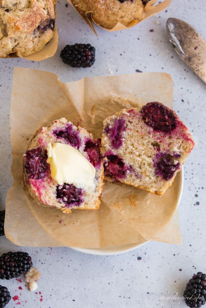 blackberry muffin on stack of white plates split open with butter in the middle and blackberries around