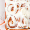 cooked and frosted pumpkin cinnamon rolls in baking dish with cinnamon sticks and linen