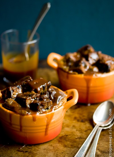 two dishes filled with pumpkin bread pudding next to two spoons and a jar of caramel sauce