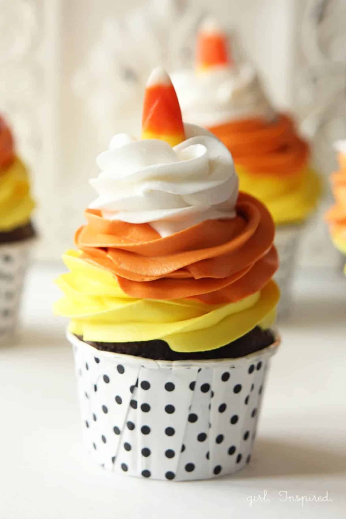 Halloween cupcake topped with swirl of yellow, orange, then white frosting and topped with a candy corn candy.