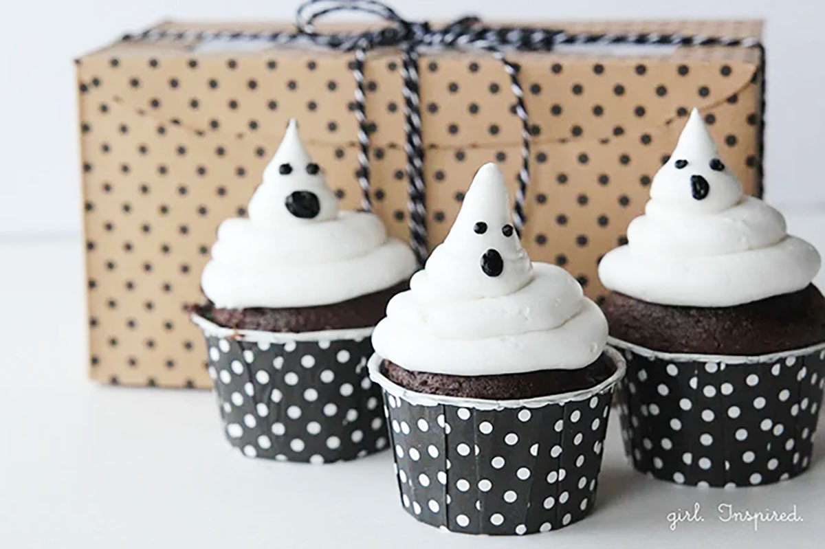 Three "ghost" cupcakes in front of a gift box.