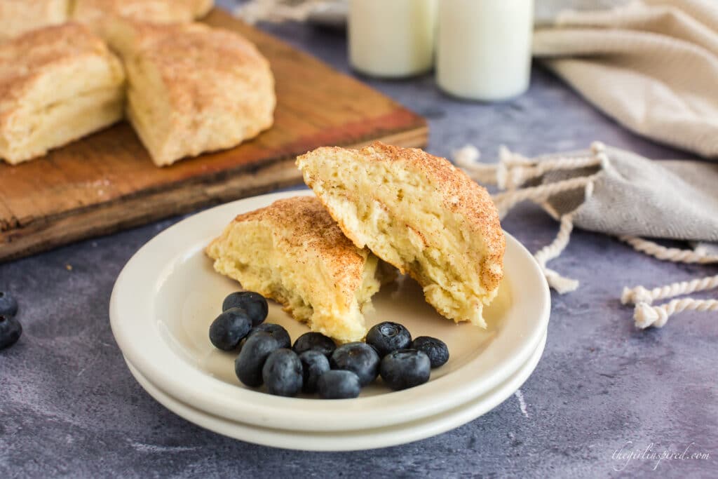 two buttermilk scones stacked on white plates with blueberries, milk and wooden board with scones in background