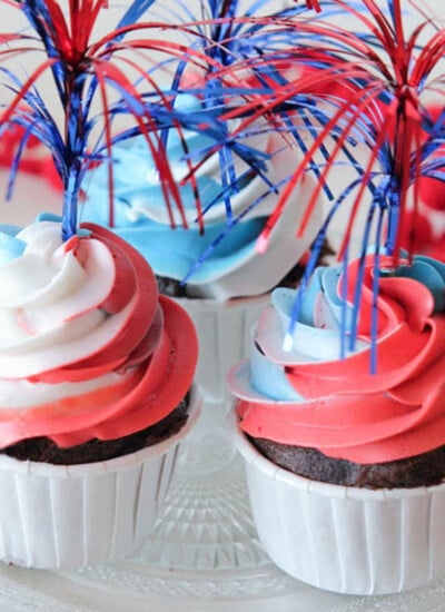 Set of three patriotic cupcakes with swirled red white and blue frosting and firecracker sparkle toppers.