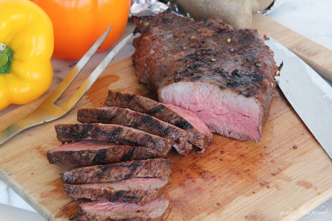 sliced steak on wooden cutting board with bell peppers in background