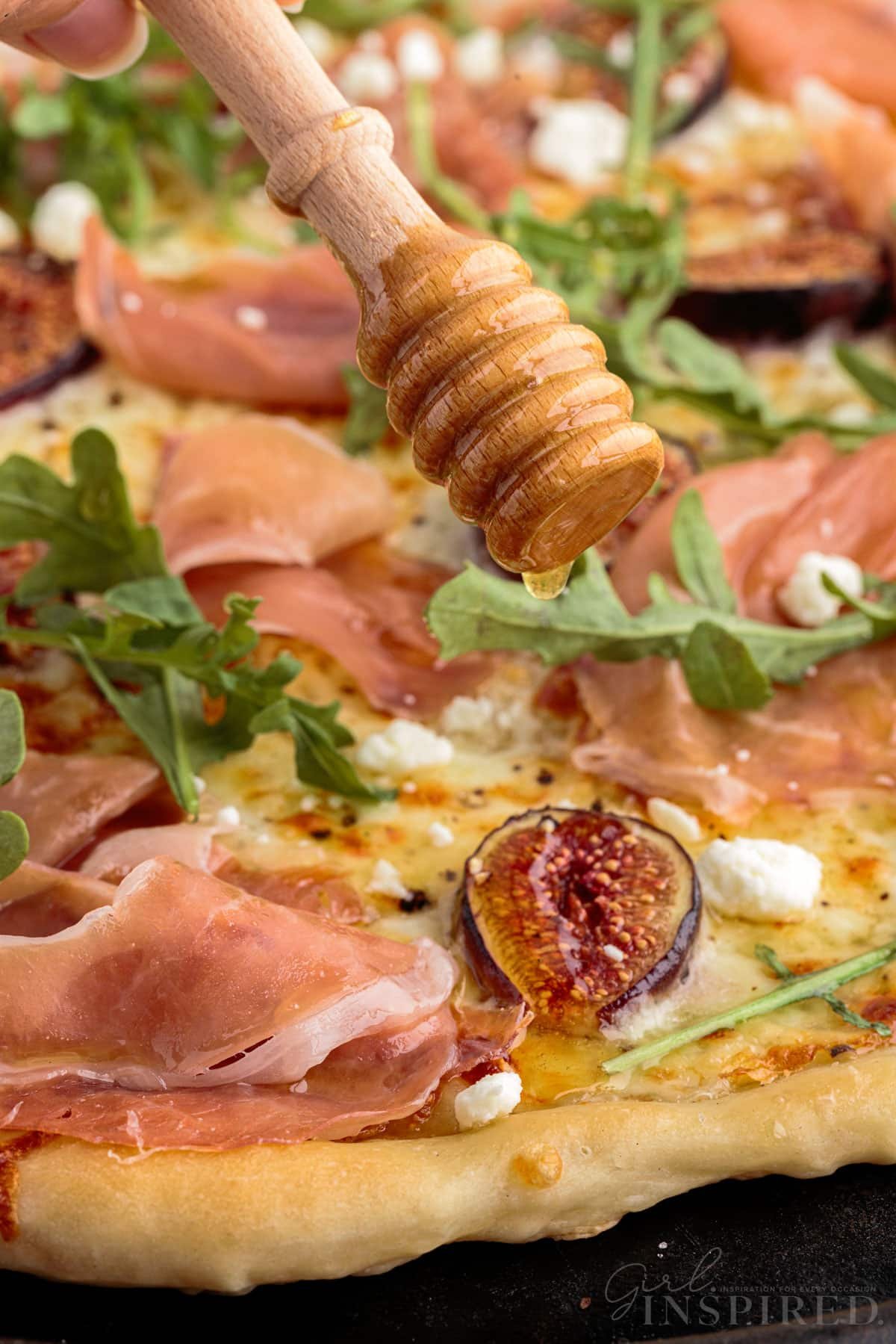 Honey dipper drizzling honey over baked fig prosciutto pizza.