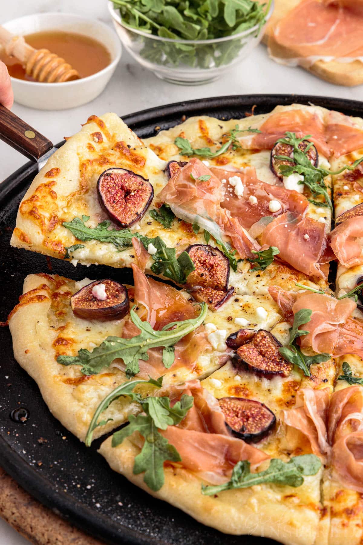 Spatula lifting slice of fig prosciutto pizza from pizza pan.