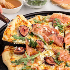 Spatula lifting slice of fig prosciutto pizza from pizza pan.