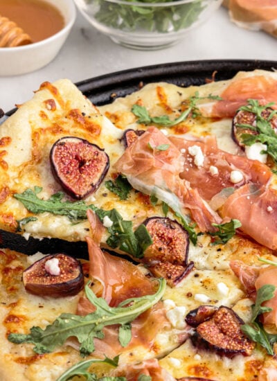 Spatula lifting slice of fig prosciutto pizza from pizza pan.